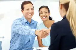Pareja sonriendo mientras estrecha la mano de una asesora al contratar un préstamo